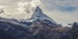 Mountain peak view from afar with cotton ball clouds covering the left part of the peak.